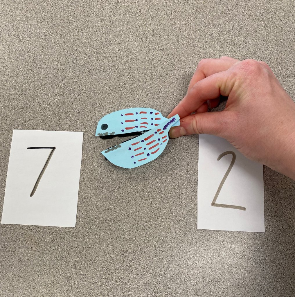 An image of a fish puppet opening its mouth towards a piece of paper with the number 7 written on it